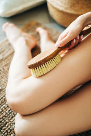 Woman holding wooden brush and doing dry massage on her feet. Self care conceptの写真素材