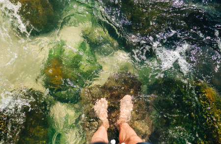Man feet standing in sea water on coral stone, top view. Summer vacation conceptの写真素材