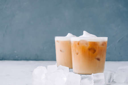 Ice brewed coffee in glass with milk foam and ice cubes on white table, copy space.の写真素材