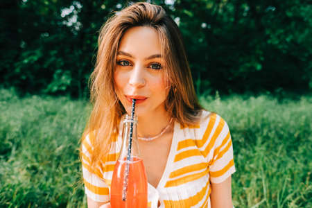 Young cheerful woman with drink, in natural park on picnic, enjoying summer holidays vacation.