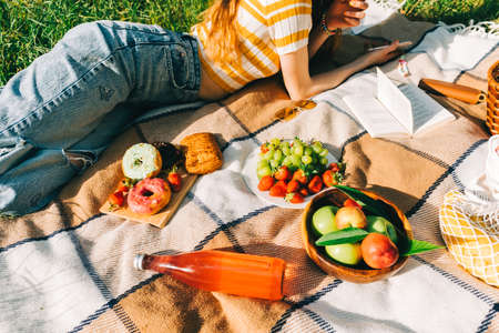 Fresh Fruits and berries, drinks and bakery on picnic blanket outdoor, summer vacation, woman lying on picnic blanket.の写真素材