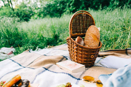 Wooden basket with fresh bread on picnic blanket in green park, summer vacations concept. Copy space