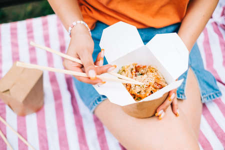 Young woman eating street food outdoor on the park, enjoying summer weather.の写真素材