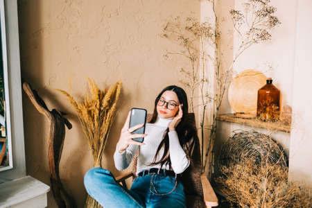 Young caucasian woman holding smartphone looking on cell using mobile phone technology at homeの写真素材