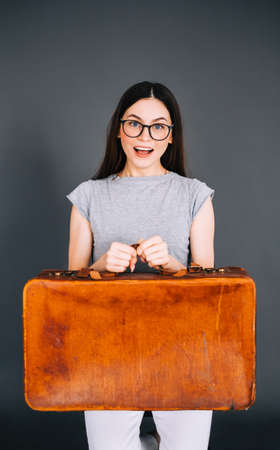 Young happy caucasian woman holding travel baggage isolated on gray background. Ready for travelingの写真素材