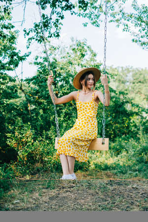 Portrait of attractive young woman in straw hat outdoors in summer sunny day on a swing.の写真素材