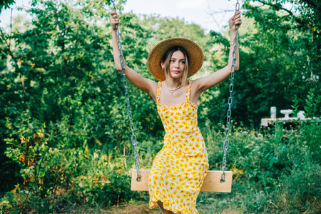 Portrait of attractive young woman in straw hat outdoors in summer sunny day on a swing.の写真素材