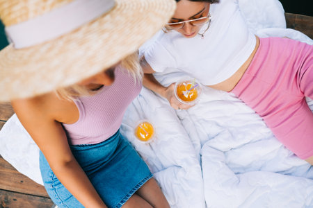 Two attractive women friends resting outdoor on lake pier, lying on white blanket.の写真素材