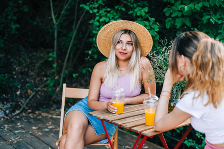 Two cheerful friends sitting on a pier lake, on summer day, communicate and drink lemonade.の写真素材