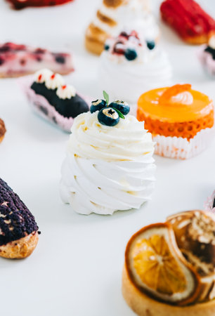 Dessert Anna Pavlova with meringue and cheese cream inside, decorated with blueberries on table with other cakes.の写真素材