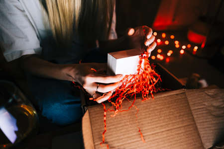 Young millennial woman open gift during video call on laptop computer and drinking wine, use...