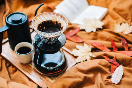Open book and brewed coffee on a bed with autumn leaves in the morning, cozy home and calm conceptの写真素材