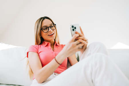 Young caucasian woman using smartphone while resting on a sofa at home.の写真素材