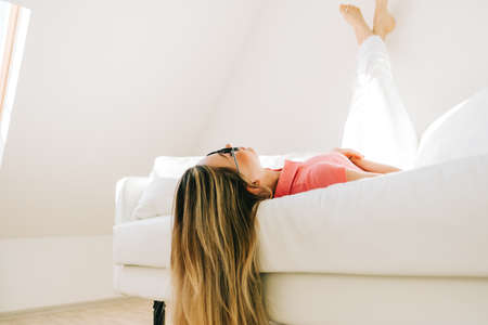 Young caucasian woman relaxed on a sofa in bright living room.の写真素材