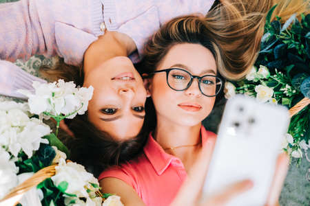 Portrait of two attractive caucasian woman lying on a floor with flowers and making selfie photoの写真素材