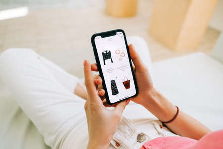 Young woman using online store app buying clothing. Woman at home lying on bed in living room using smartphone buys clothings in internet shop.の写真素材