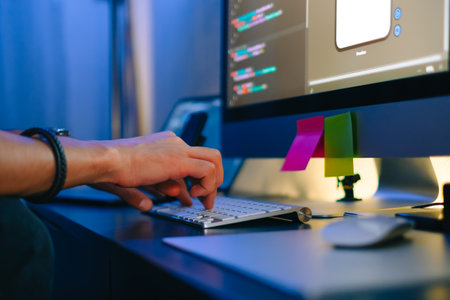 Mobile developer writes program code on a computer, typing on keyboard, programmer work in home...