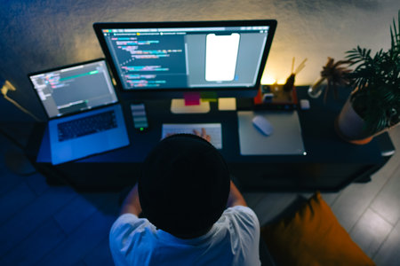 Young man mobile developer writes program code on a computer, programmer work in home office.の写真素材