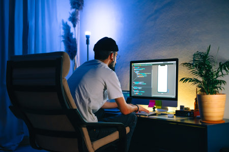 Young man mobile developer writes program code on a computer, programmer work in home office.の写真素材