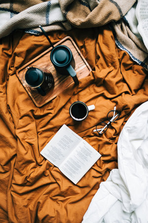 Coffee brewed in a pour over and kettle on a wooden board with open book in bed. Morning at home, coziness and comfort.の写真素材