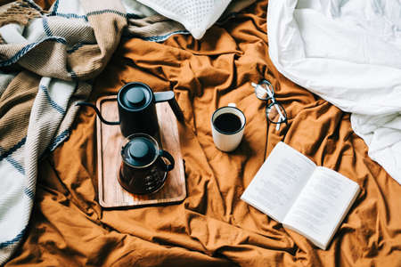 Coffee brewed in a pour over and kettle on a wooden board with open book in bed. Morning at home, coziness and comfort.の写真素材