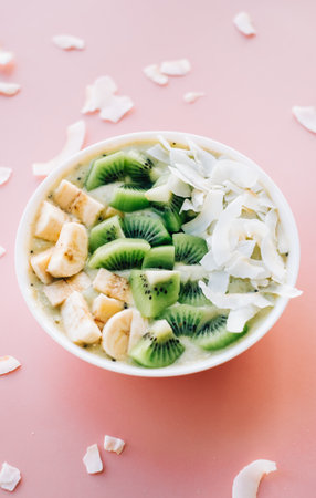 Healthy fruit smoothie bowl with banana, coconut and kiwi on pink background.の写真素材