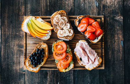 Delicious healthy toasts mix for breakfast, lunch or snack on a wooden board in hands.の写真素材