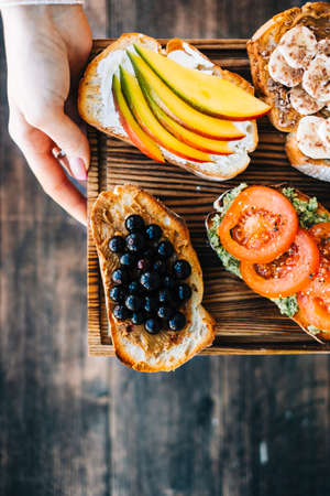 Delicious healthy toasts mix for breakfast, lunch or snack on a wooden board in hands.の写真素材