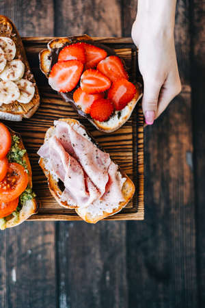 Delicious healthy toasts mix for breakfast, lunch or snack on a wooden board in hands.の写真素材