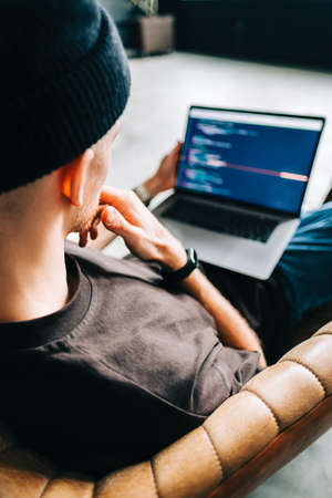 Young man mobile developer writes program code on a computer, programmer work in home office.の写真素材