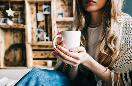 Drinking hot drink in cozy winter atmosphere, woman sitting on a floor in living room with Christmas decoration.の写真素材