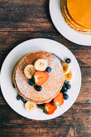 Tasty pancakes with strawberry, blueberry and banana in a white plate on the table.の写真素材