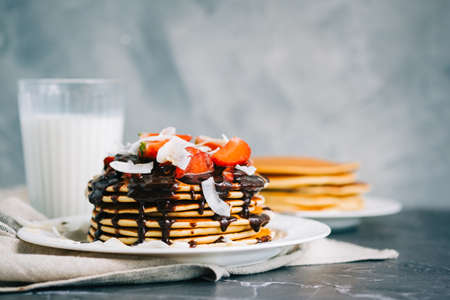 Tasty pancakes with strawberry, coconut chips and hot chocolate in a white plate on the table.の写真素材