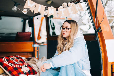 Portrait of young caucasian woman sitting in a car in winter day, during traveling on a van and enjoying holiday.の写真素材