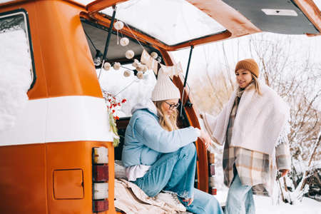 Portrait of two cheerful women friends sitting in a van in winter camp, enjoying holiday.の写真素材