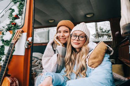 Portrait of two cheerful young women friends sitting in a van in winter camp.の写真素材