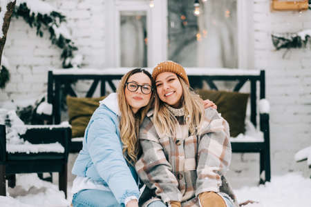 Portrait of two cheerful women friends sitting outdoor on the backyard after snowfall, enjoying winter time.の写真素材