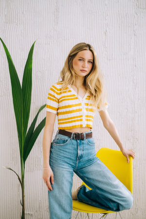 Portrait of attractive stylish caucasian young woman with blonde hair posing near yellow chair.の写真素材