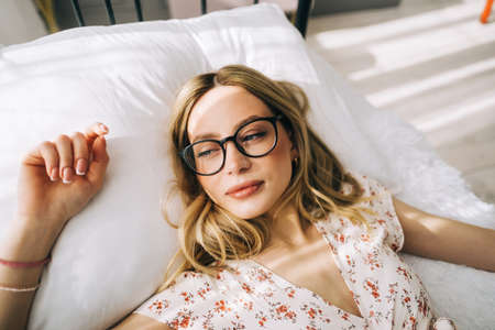 Portrait of young attractive happy woman in eyeglasses lying on a bed.の写真素材