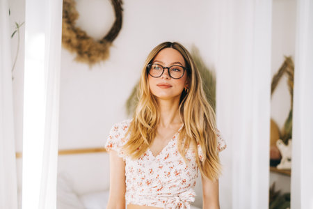 Portrait of attractive caucasian young woman in eyeglasses standing in a bright bedroom in resort.の写真素材