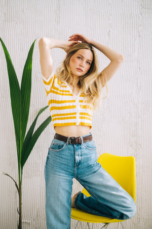 Portrait of attractive stylish caucasian young woman with blonde hair posing near yellow chair.の写真素材