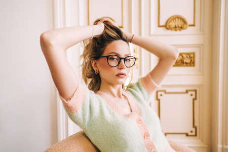 Portrait of attractive caucasian young woman in eyeglasses sitting on armchair in bright living room near ornamental door.の写真素材