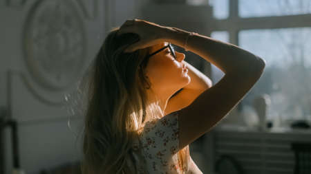 Young attractive caucasian woman shakes long blonde straight hair in sunset light at home.の写真素材