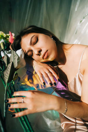 Portrait of attractive caucasian woman in silky dress, sitting near table in a sunny room with flowers on a wall.の写真素材