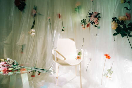 Empty white chair in sunny room with flowers on a wall.の写真素材