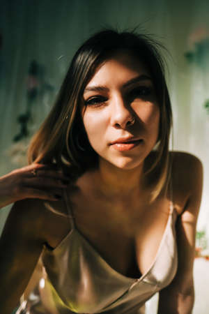 Portrait of attractive caucasian woman in silky dress, sitting in a sunny room with flowers on a wall.の写真素材