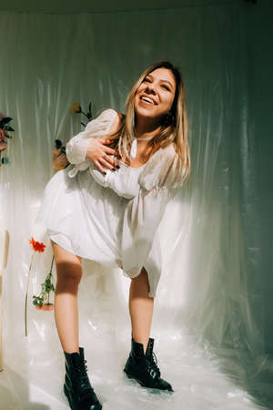 Portrait of attractive caucasian woman in short white dress, posing in a sunny room with flowers on a wall.の写真素材