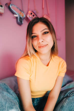 Portrait of young attractive cheerful woman sitting in a bedroom with pink walls.