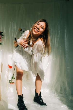 Portrait of attractive caucasian woman in short white dress, posing in a sunny room with flowers on a wall.の写真素材