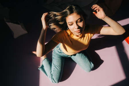 Portrait of young attractive caucasian woman shaking hair, sitting on a floor in a bedroom in sunlight.の写真素材